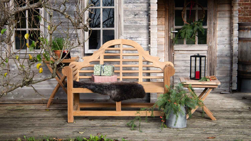 Teak bench on a wooden deck with a rustic building in the background