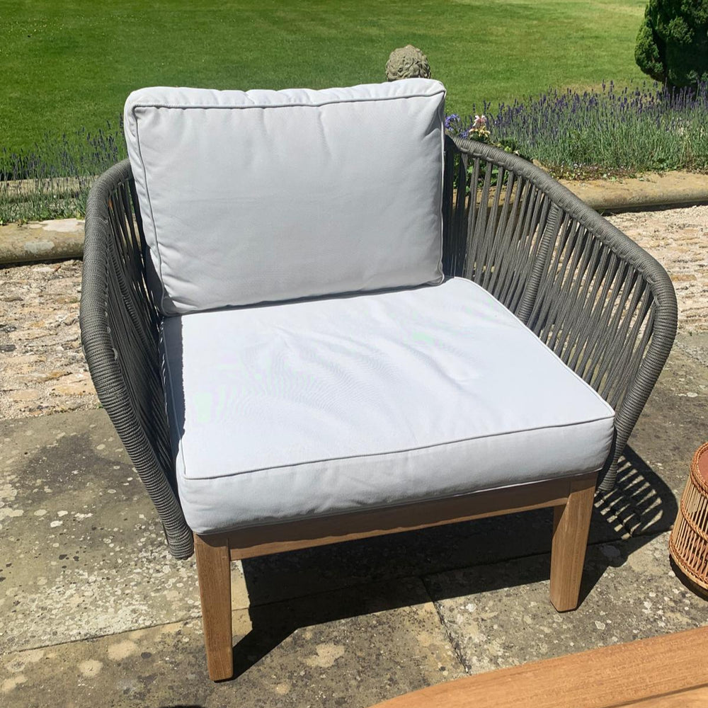 
                  
                    Teak and rope outdoor armchair with cream cushions in garden setting. 
                  
                