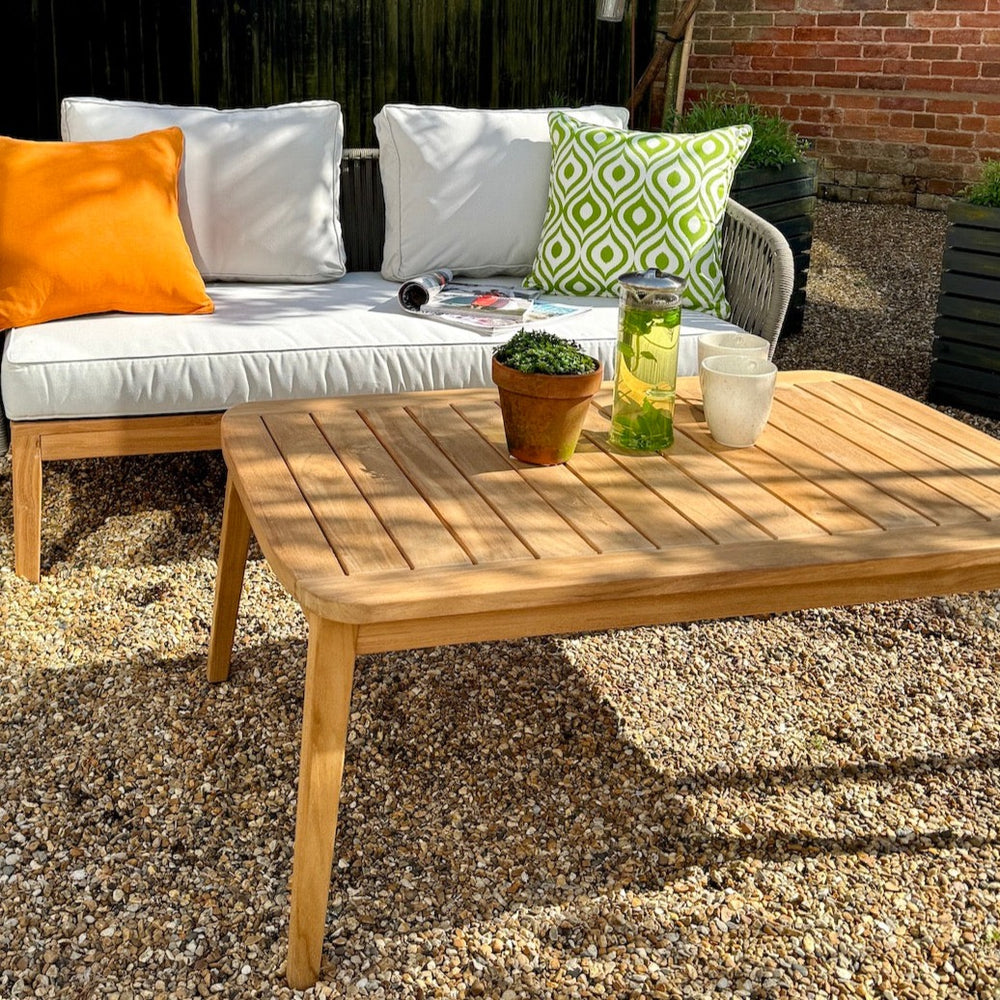 
                  
                    Teak outdoor sofa with white seat and back cushions and colourful scatter cushions, with teak table in front, set with cups and plant pots. 
                  
                