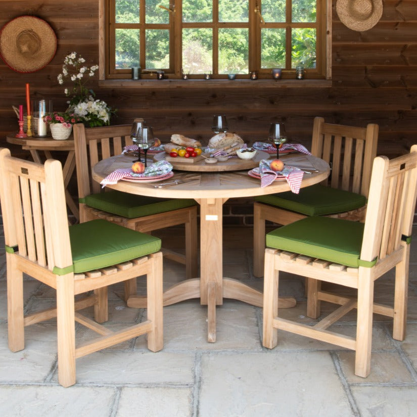 A teak dining set with a round teak dining table and green cushioned chairs placed on a patio, indoors.