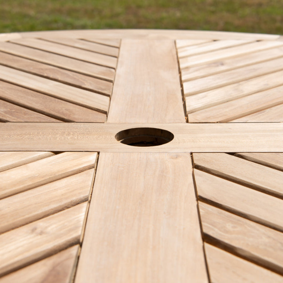 
                  
                    Close up of round teak dining table with slatted top, central bar and hole for parasol
                  
                