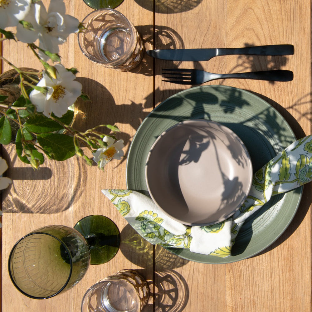 
                  
                    Close up of teak tabletop with place setting, flowers and glasses.  
                  
                