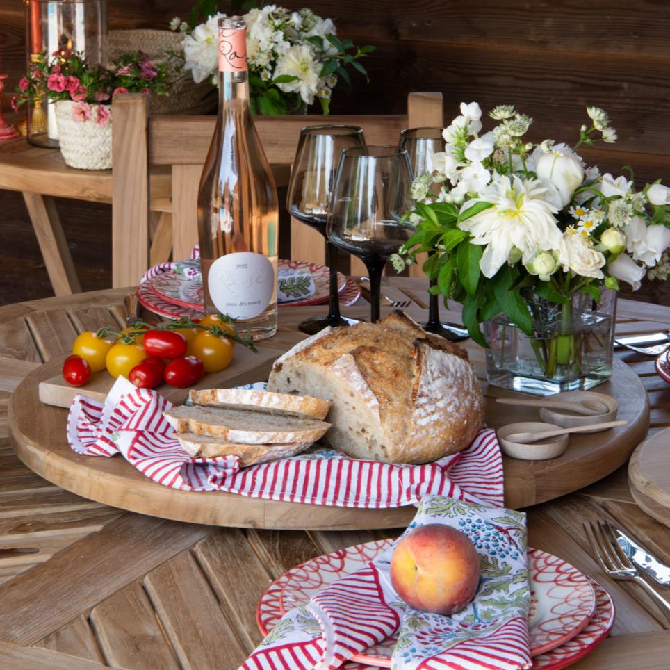 
                  
                    A 'lazy susan' turntable made of teak, displayed with food and drink on a table, surrounded by outdoor seating and decor.
                  
                