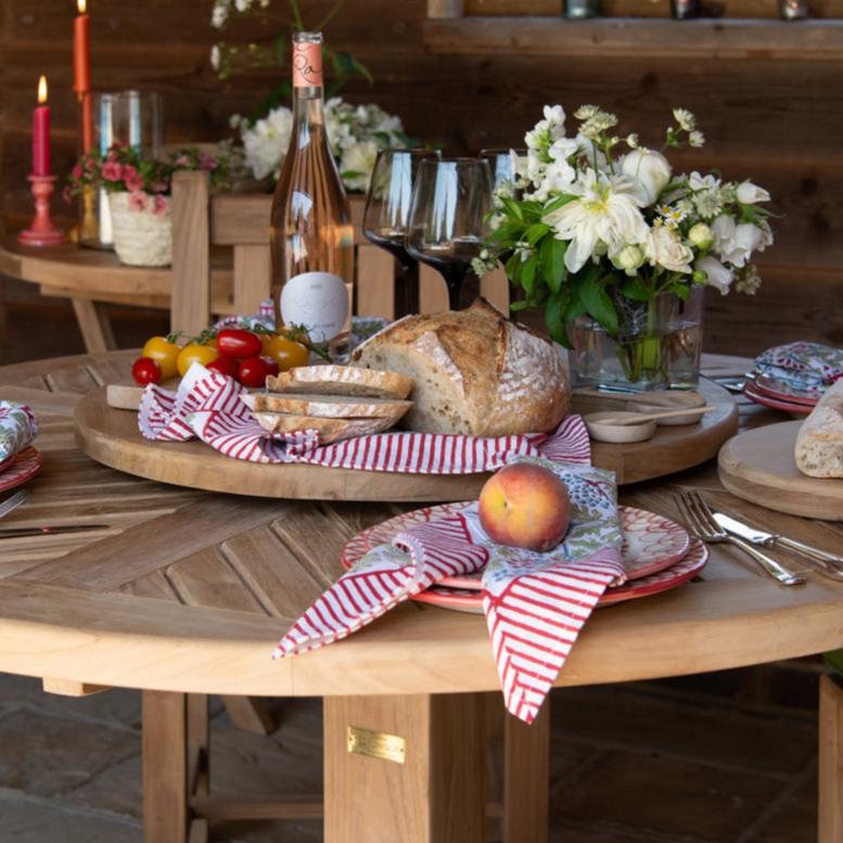 
                  
                    Round 'Lazy Susan' turntable set with food and drinks, on a round teak table with place settings and flower arrangements. 
                  
                