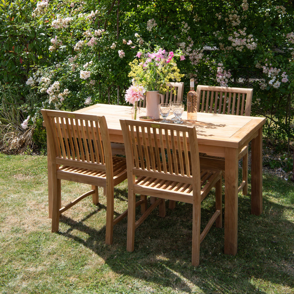 Teak outdoor dining set with chairs and a table in a garden setting with flowers and greenery.