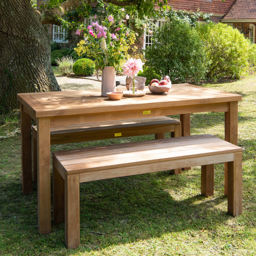 Teak outdoor dining set with rectangular table and benches, in garden setting. 