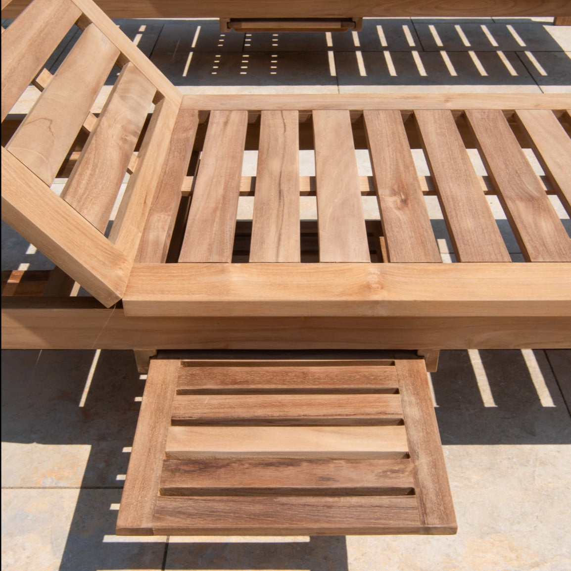 Side view of teak reclining chair, angled to demonstrate seated position, with extendable panel table, on stone patio