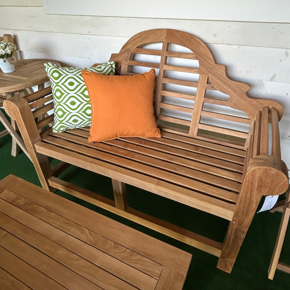 
                  
                    Teak bench with decorative pillows, with teak tables in front and to the side, in a patio setting
                  
                