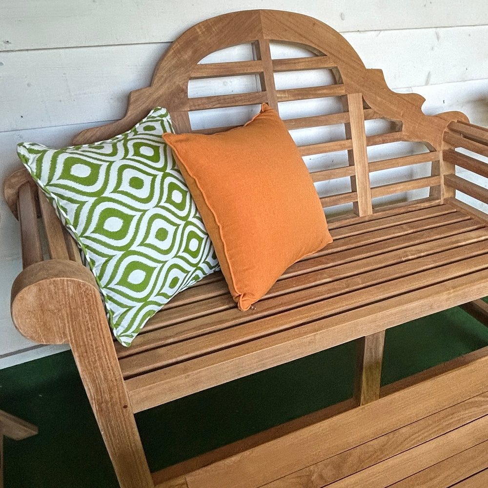 
                  
                    Teak bench with green and orange patterned cushions and teak table in front,  against a white wall.
                  
                