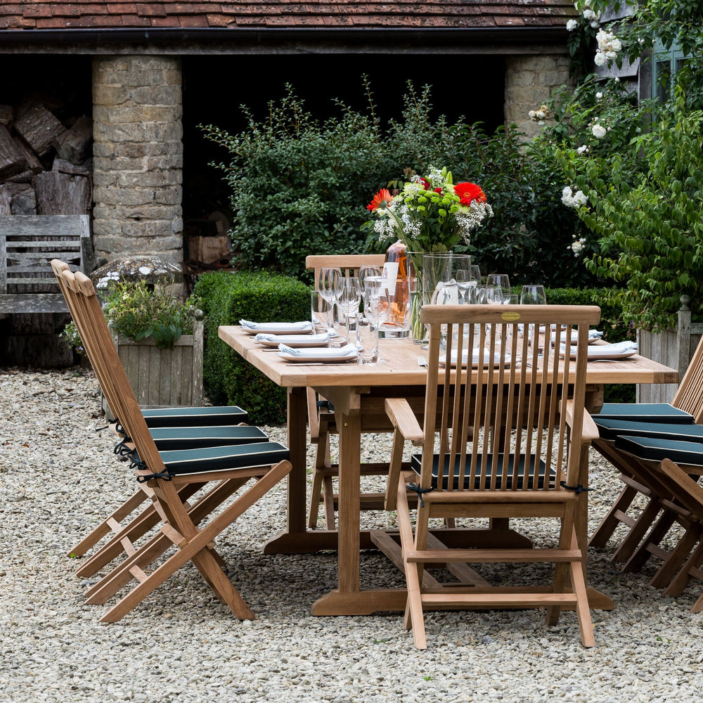 
                  
                    Teak outdoor dining set with table and chairs in a garden setting.
                  
                