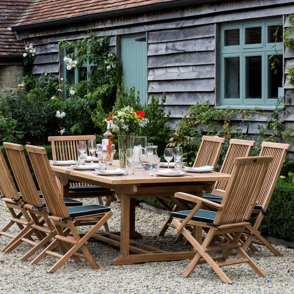 
                  
                    Teak outdoor dining set with table and chairs in front of a rustic building.
                  
                