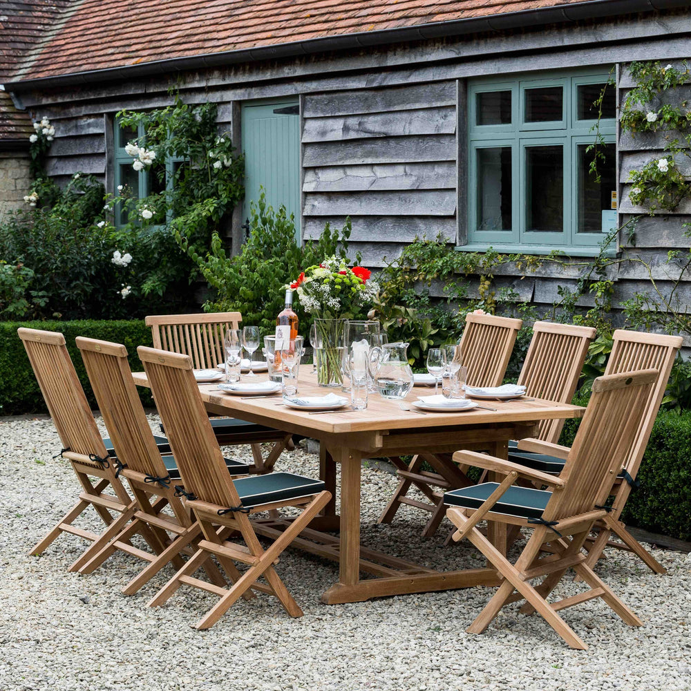 
                  
                    Teak outdoor dining set with chairs and table in front of a rustic building.
                  
                
