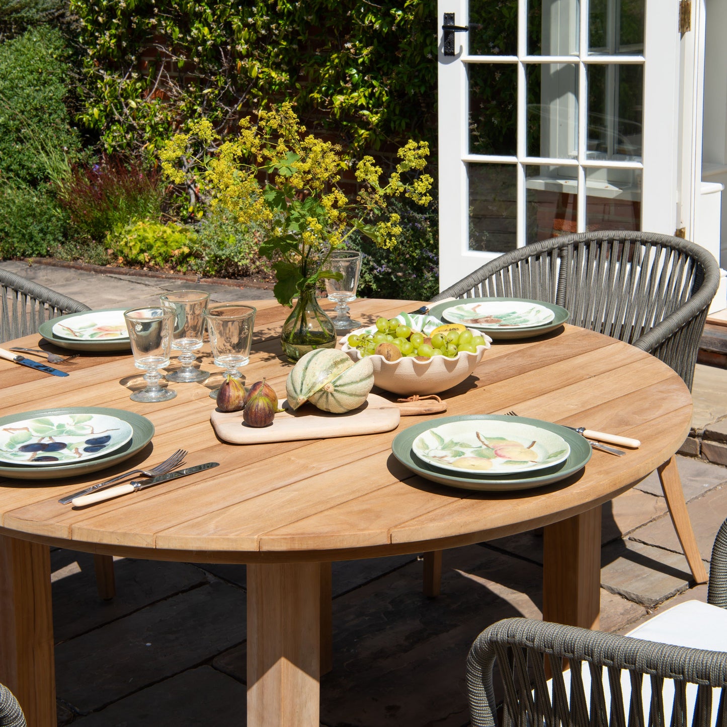 Round teak outdoor dining table set with teak chairs on a patio