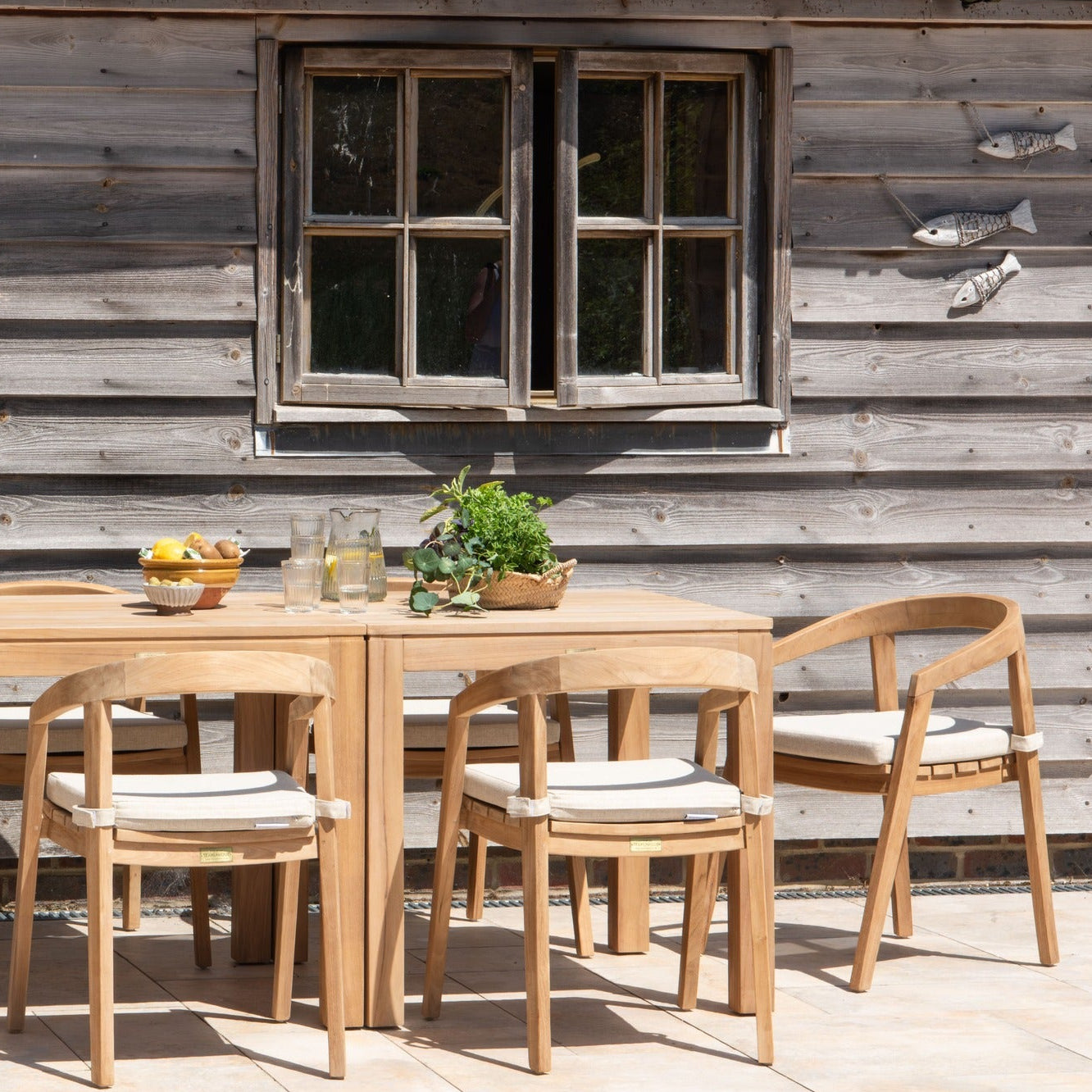 Teak outdoor dining set with rectangular teak table and chairs in front of a wooden cabin.