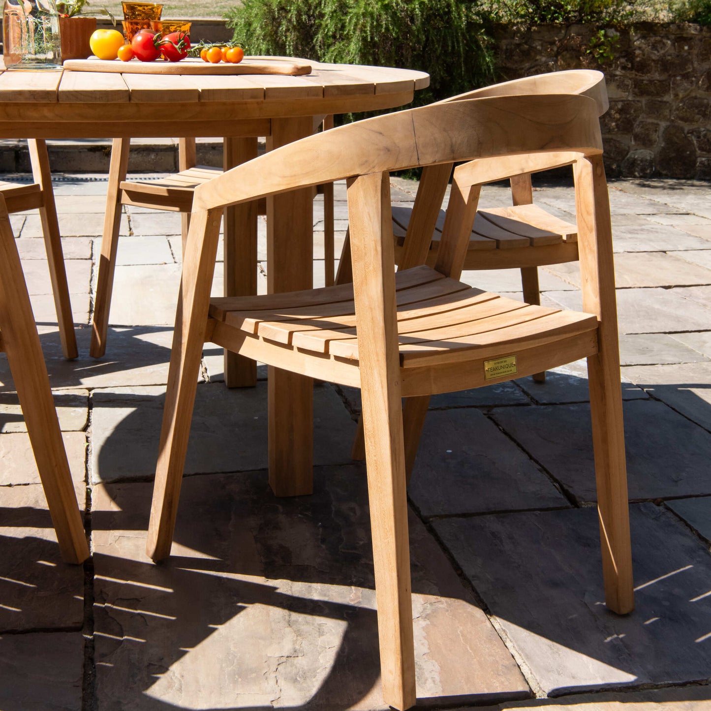 Teak wooden outdoor table and chairs with teak chopping board with vegetables, on a stone patio