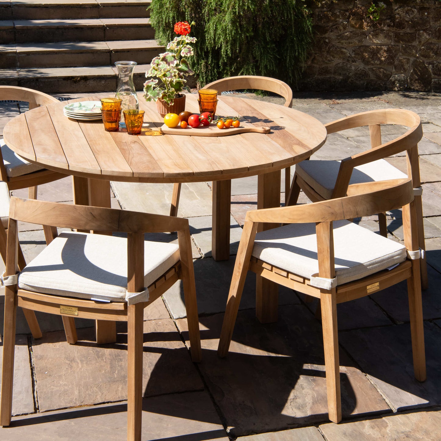 Teak wooden outdoor dining table with teak chairs in a garden setting.