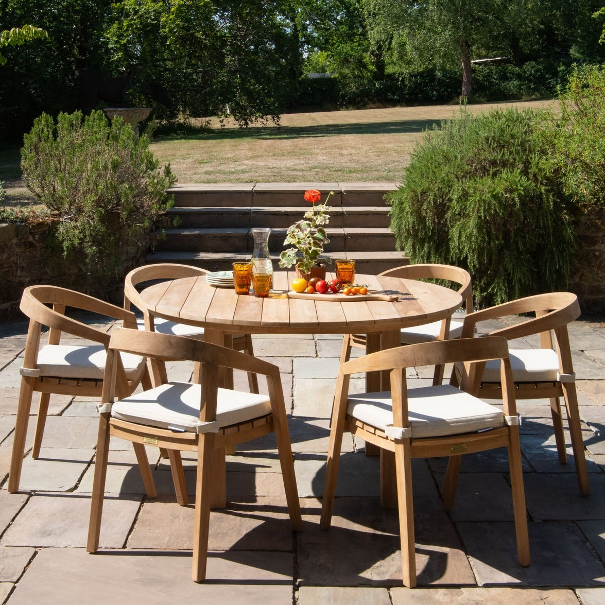 Outdoor patio with teak wooden furniture and a teak round table in a garden setting.