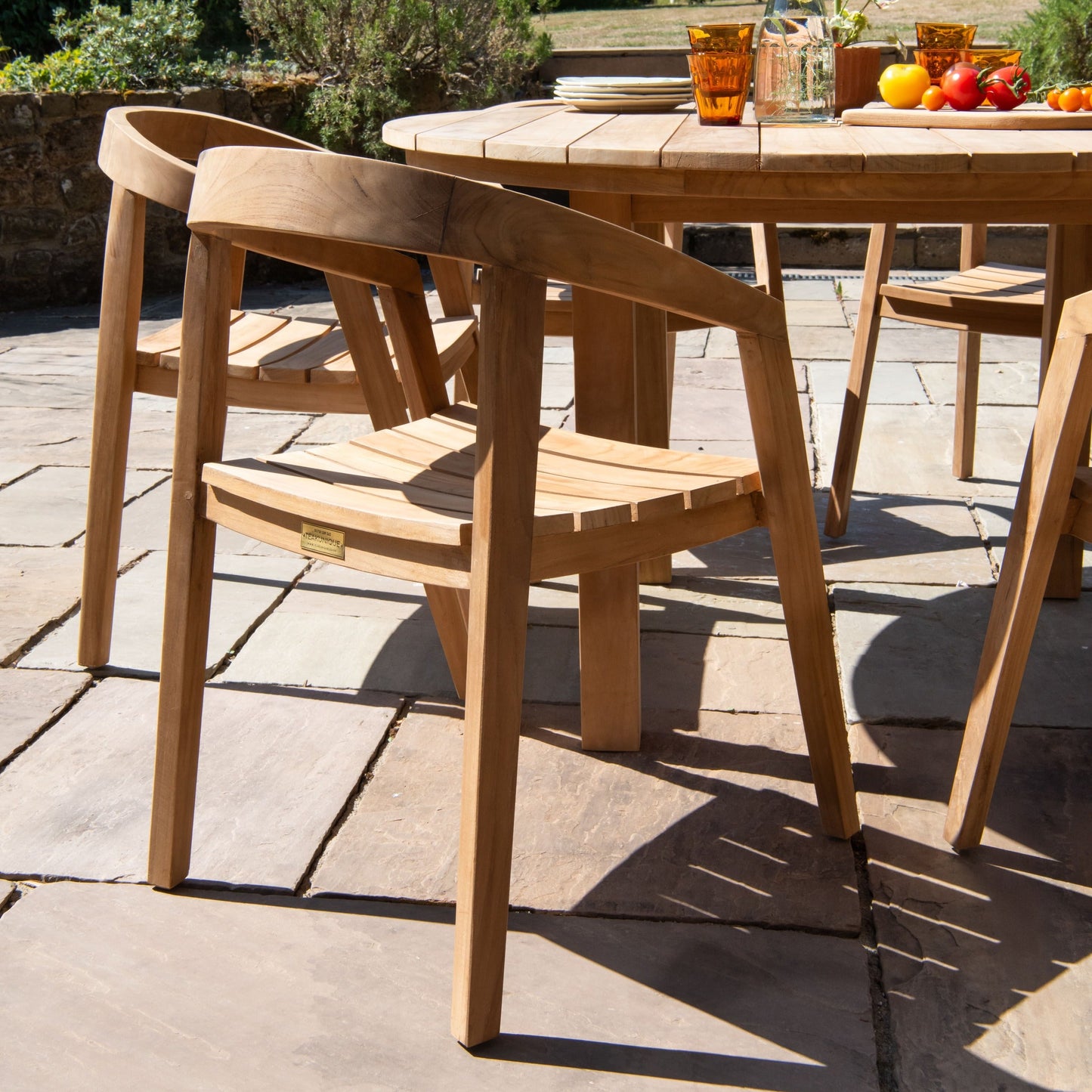 Teak wooden outdoor table with chairs and a fruit platter on a sunny day.