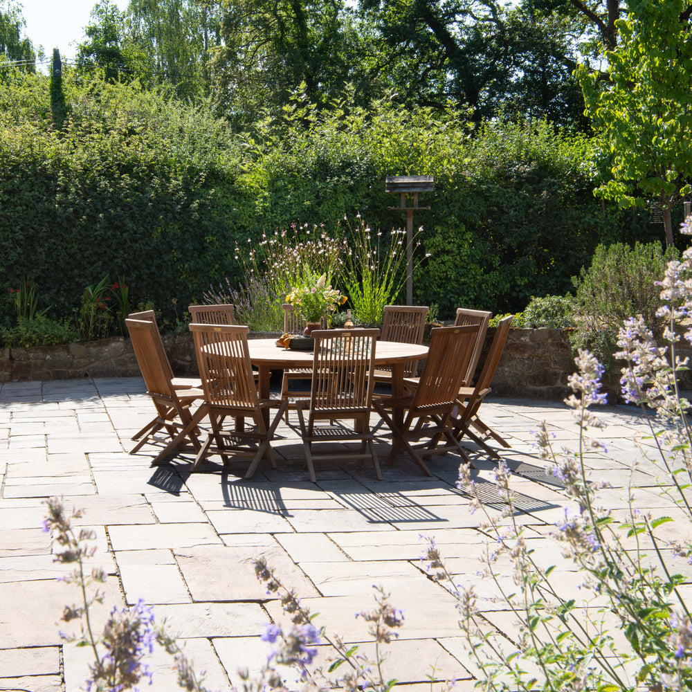 
                  
                    Outdoor patio with teak dining set surrounded by greenery
                  
                