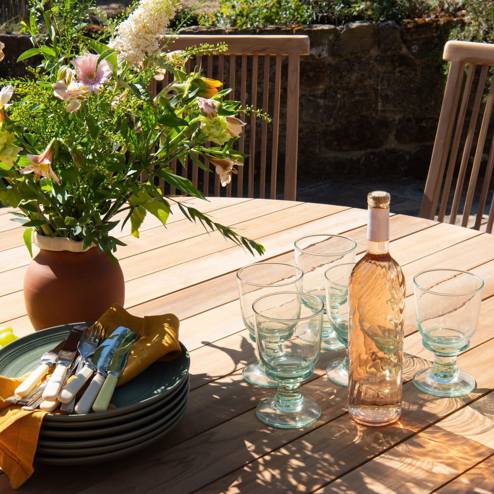 
                  
                    Teak outdoor table setting with wine, glasses, and flowers on a patio.
                  
                