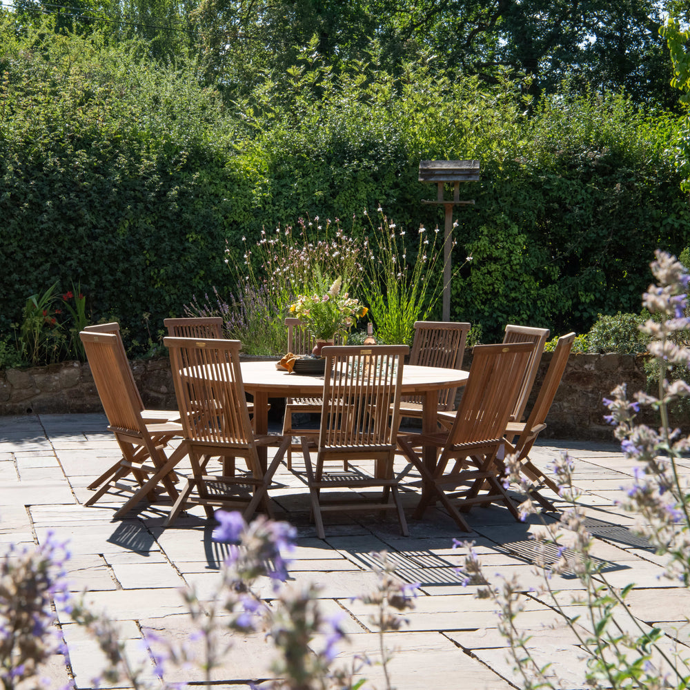 Teak outdoor dining set on a patio with garden and trees in the background