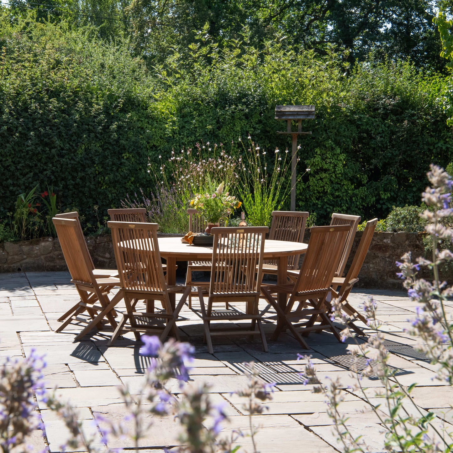 Teak outdoor dining set on a patio with garden and trees in the background