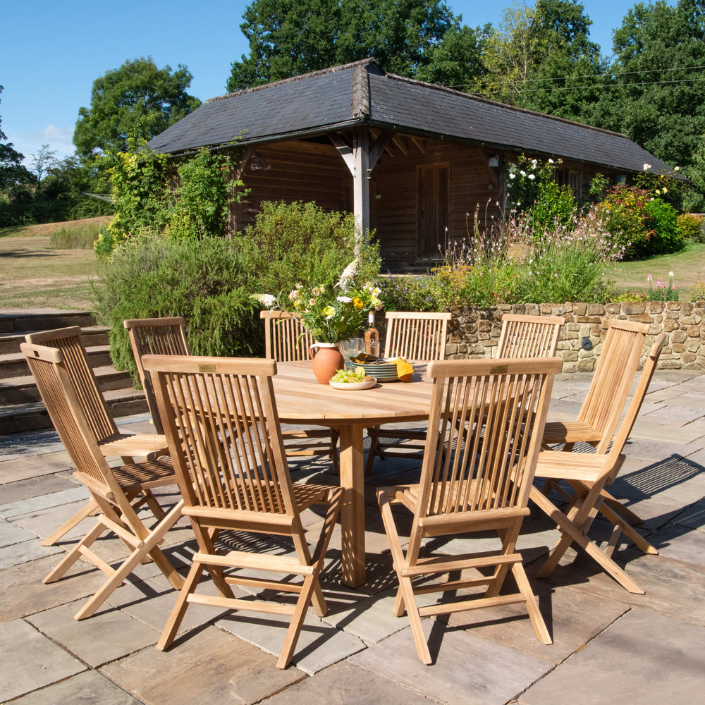 Outdoor teak dining set on a patio with a garden and gazebo in the background