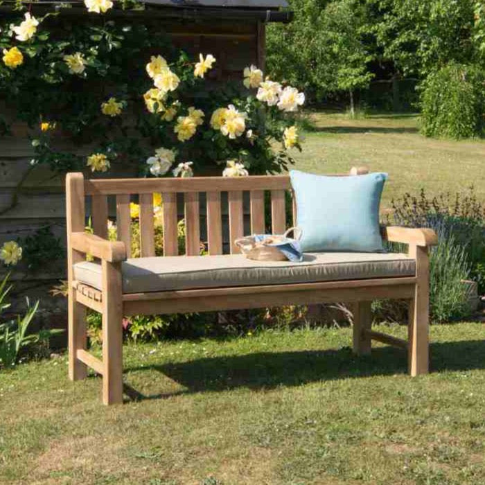 
                  
                    Classic teak bench with square backrest and legs, with stone coloured seat pad and blue cushion, in garden setting. 
                  
                