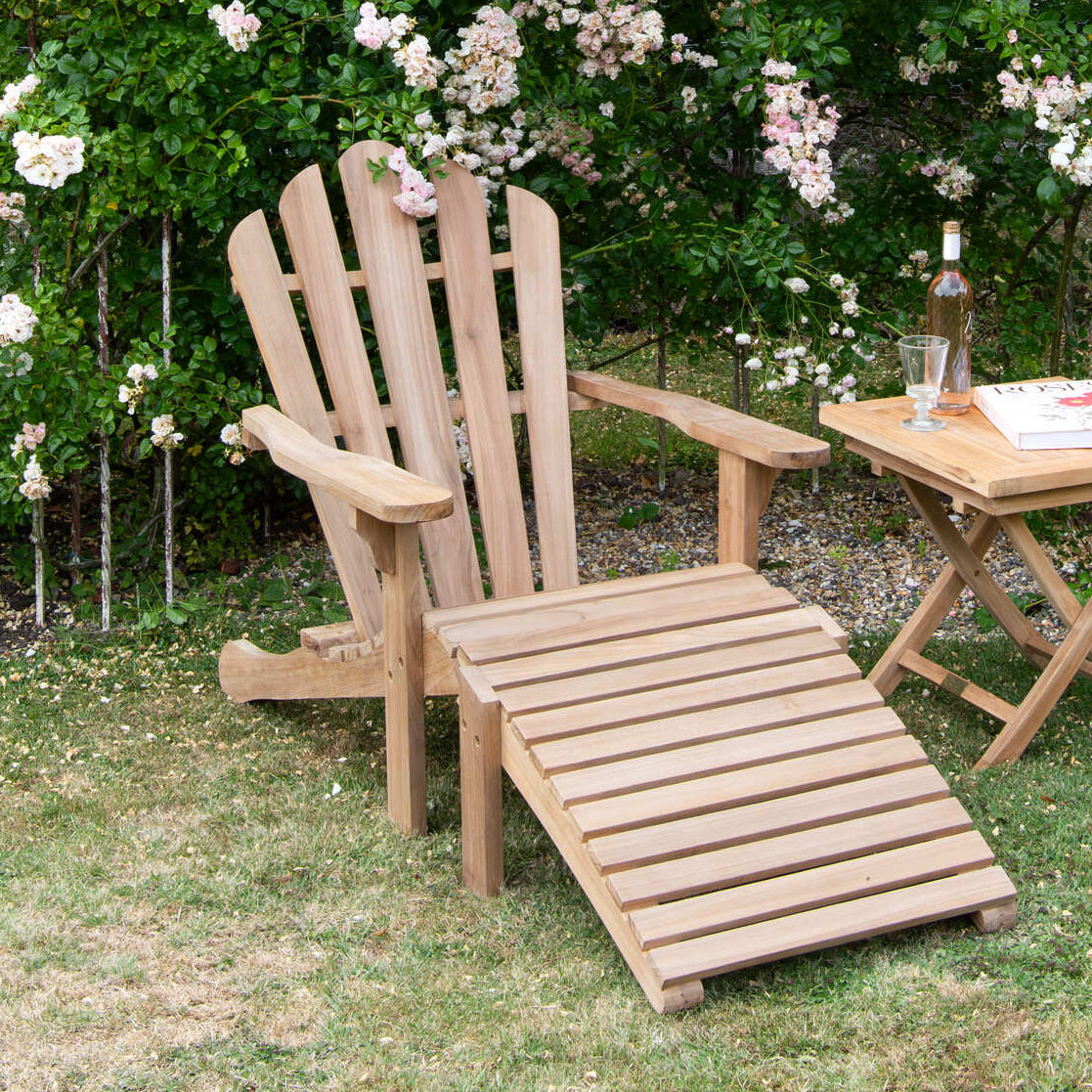 Teak wooden Adirondack chair and table set in a garden with white flowers and greenery.