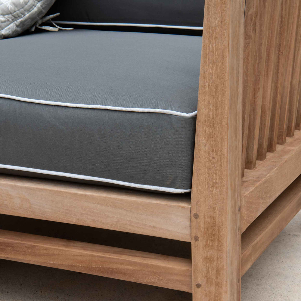 
                  
                    Close up of corner of teak outdoor sofa section with dark grey and white cushion. 
                  
                