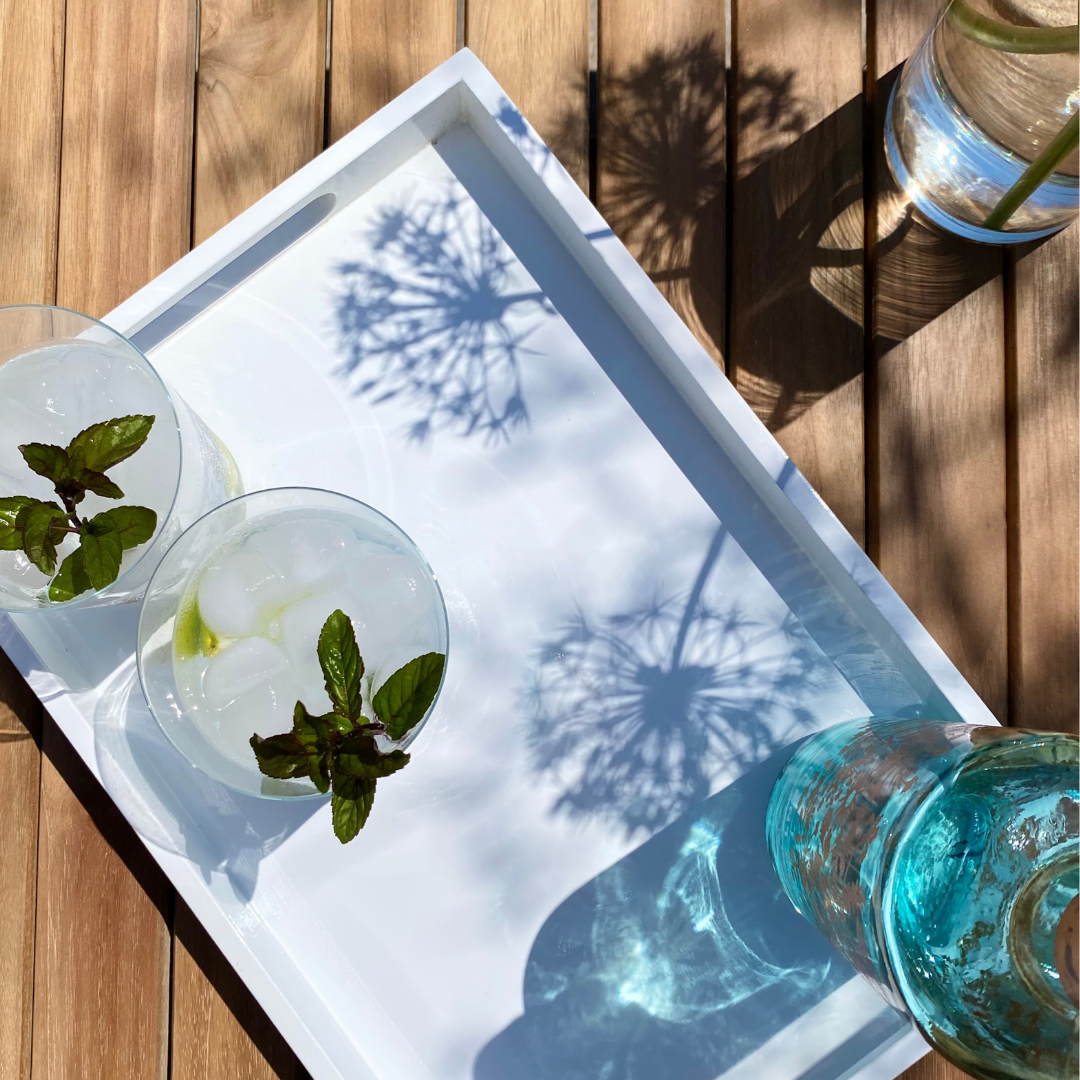 overhead shot of teak table top with white tray of glasses, blue bottle and a vase of flowers on one side.  