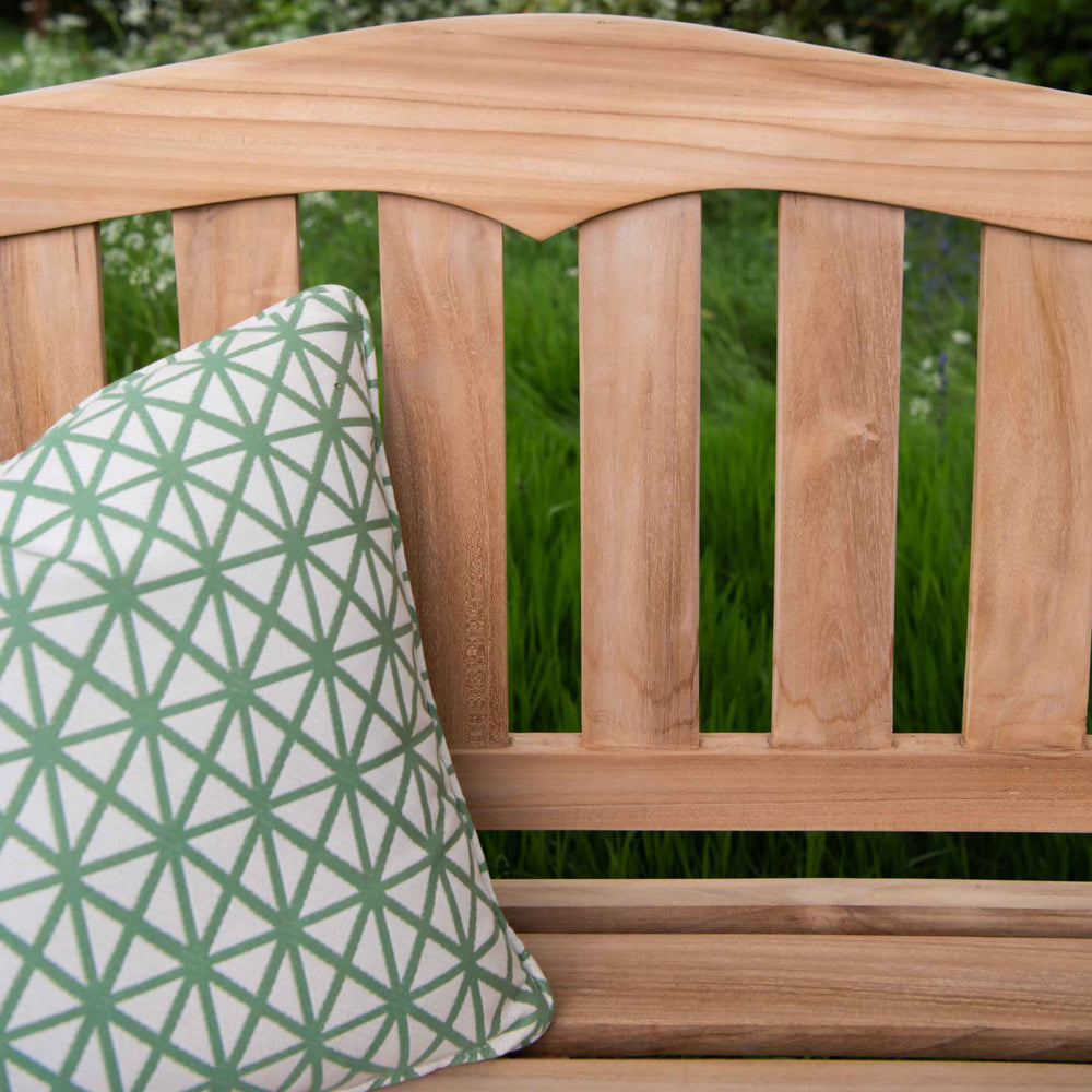 
                  
                    Close up of backrest of teak bench with curved top rail and green patterned cushion. 
                  
                