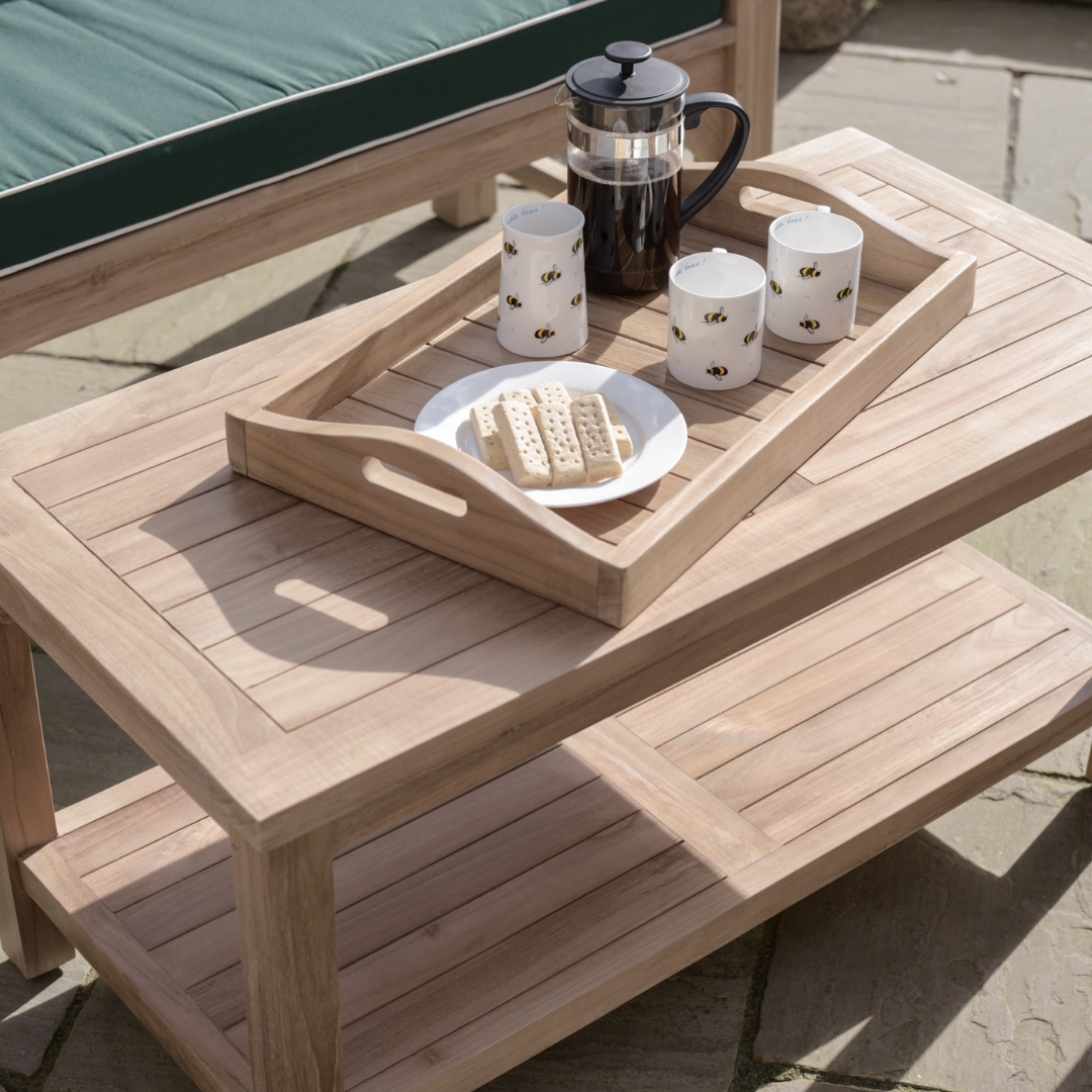 Teak rectangular coffee table with shelf below,  with teak tray of cups and coffee, in front of teak sofa with green seat cushion.  