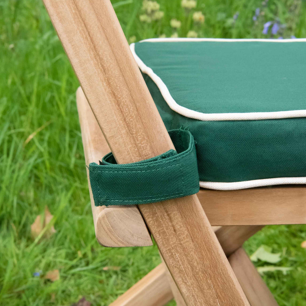 
                  
                    Close up of side view of teak folding chair with green and white seat cushion tied to back rest, on grassy surface 
                  
                
