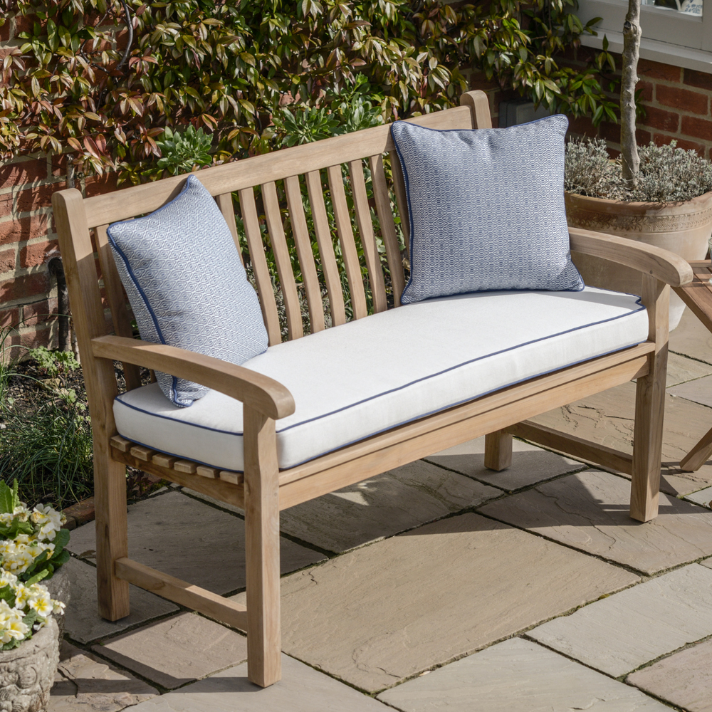 
                  
                    Teak bench with slatted backrest and curving armrests, with cream coloured seat cushion and blue scatter cushions, on patio with ceramic planters.  
                  
                