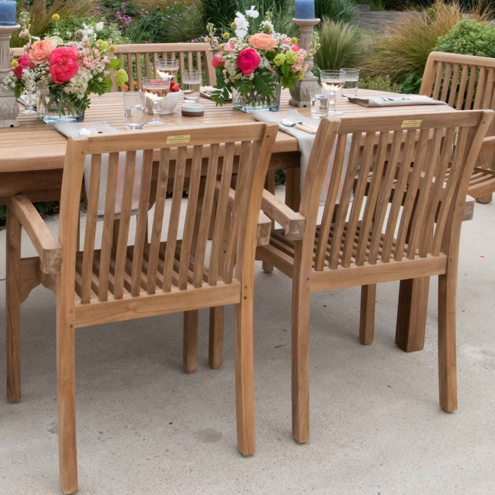
                  
                    Teak outdoor dining table and armchairs on a stone patio. The table has flower arrangements, glasses and place settings.  
                  
                