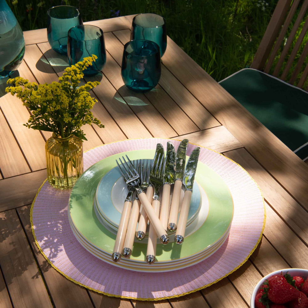 
                  
                    Close up of tabletop of teak folding rectangular table with stack of pastel coloured plates and cutlery and green glasses
                  
                