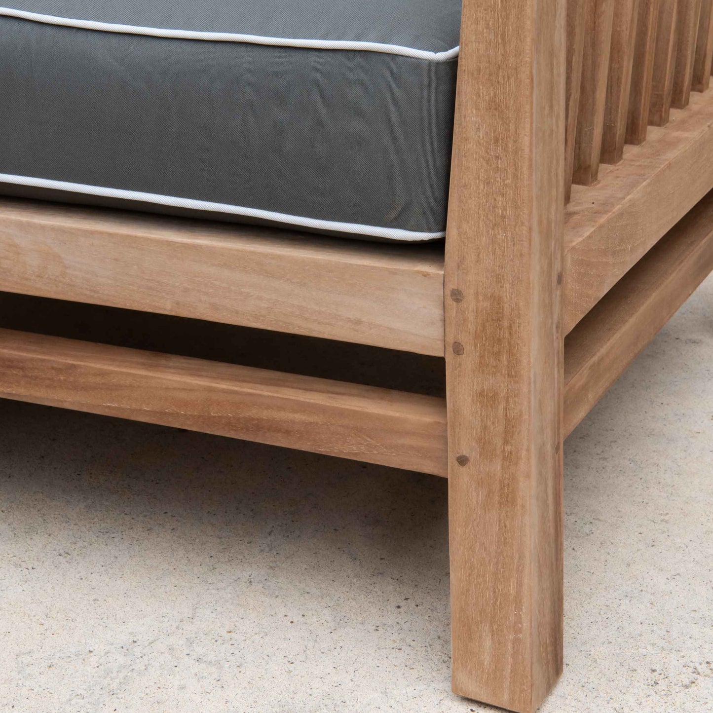 Corner shot of teak sofa section with grey-green cushion with white piping. 
